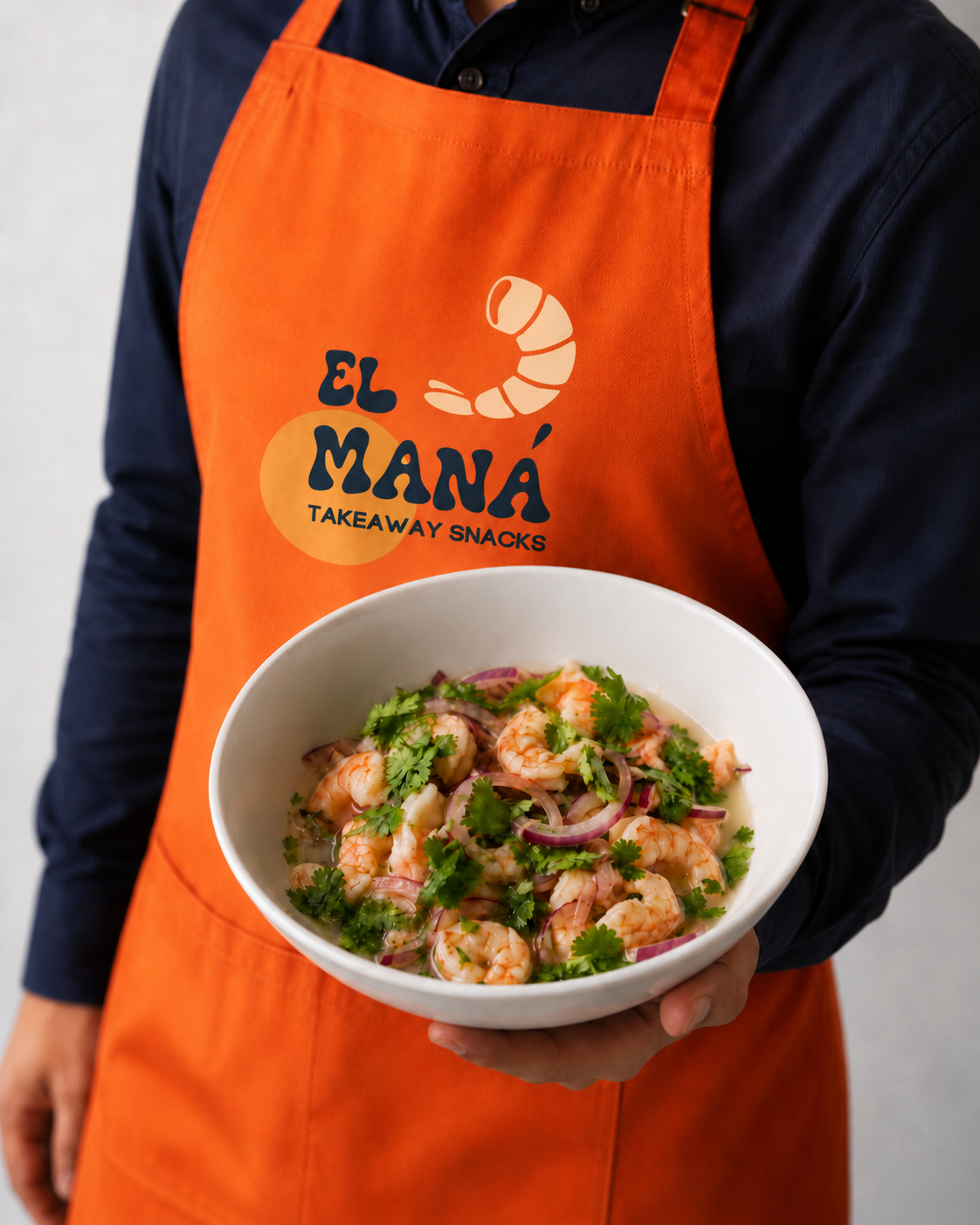 Persona con delantal naranja de El Maná Takeaway sosteniendo un bol de gambas frescas